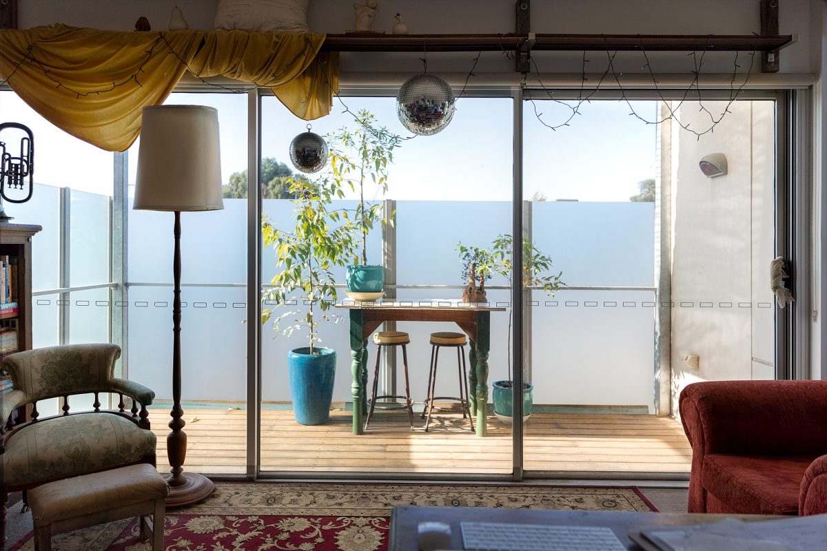 Housing Co-operative Murundaka showcases how transformative change is possible in the suburbs of Melbourne | A view from inside apartment looking out at the wooden sunny balcony with table and chairs | Co-op living Australia | cohousing collective | Photography by Jasmine Fisher | edited by Jana Perković | Assemble Papers